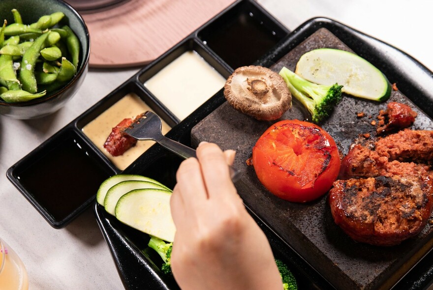 A hand using a fork to dip meat from a platter into a tray of dips.
