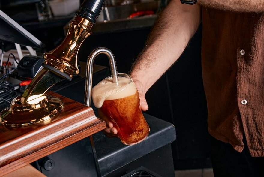 Hand holding a beer glass being filled under a tap.