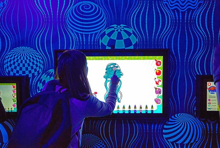 Child colouring in a jellyfish drawing on a display screen.