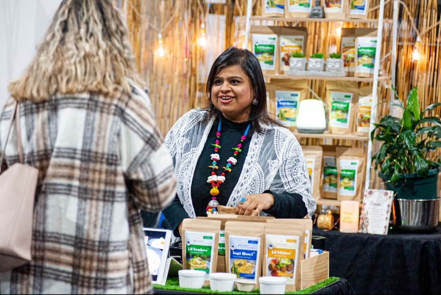 Stallholder interacting with a customer over a market stall selling vegan produce.