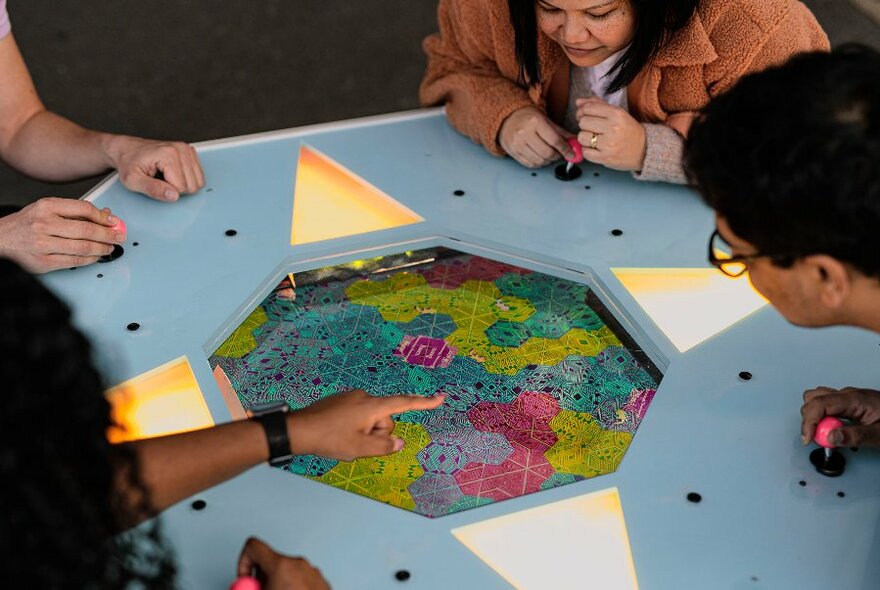 People leaning over a games table pointing at a coloured octagon.