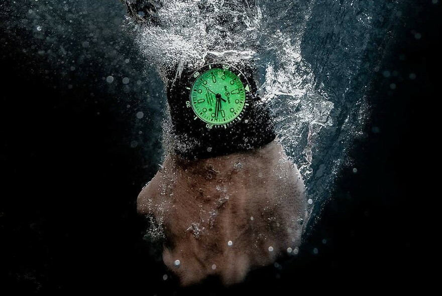 A hand being immersed in water wearing a luminous green waterproof watch.