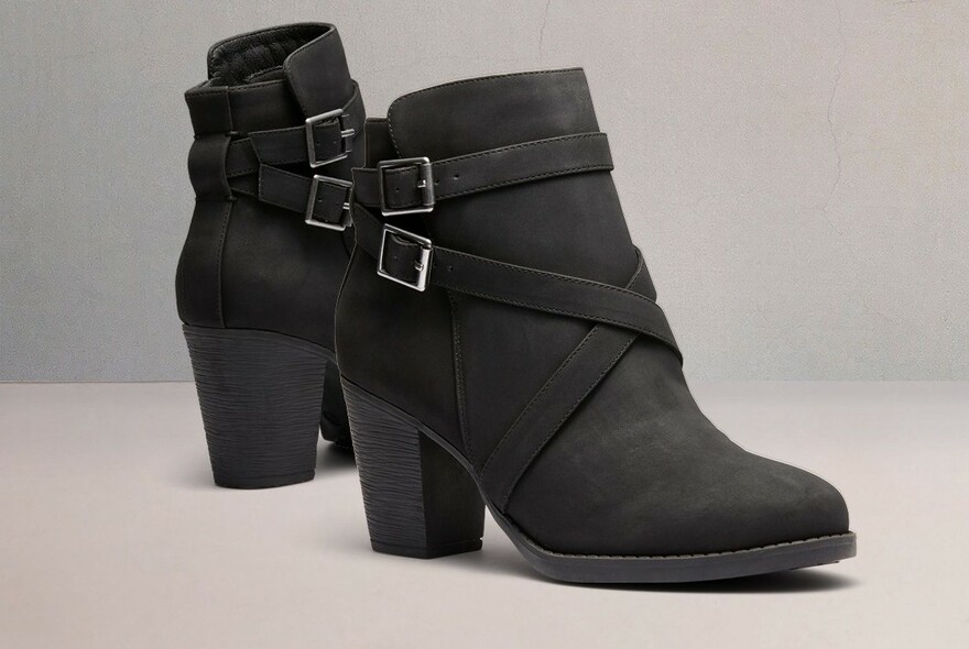 A pair of black high-heeled ladies boots with straps and buckles.