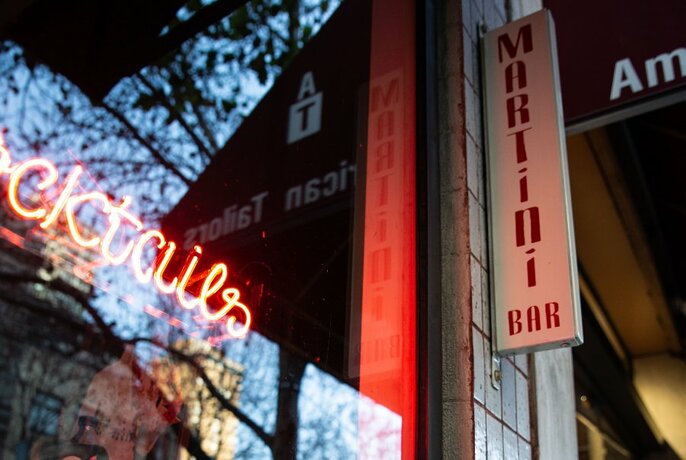 A martini bar with a neon red cocktail sign in the window.