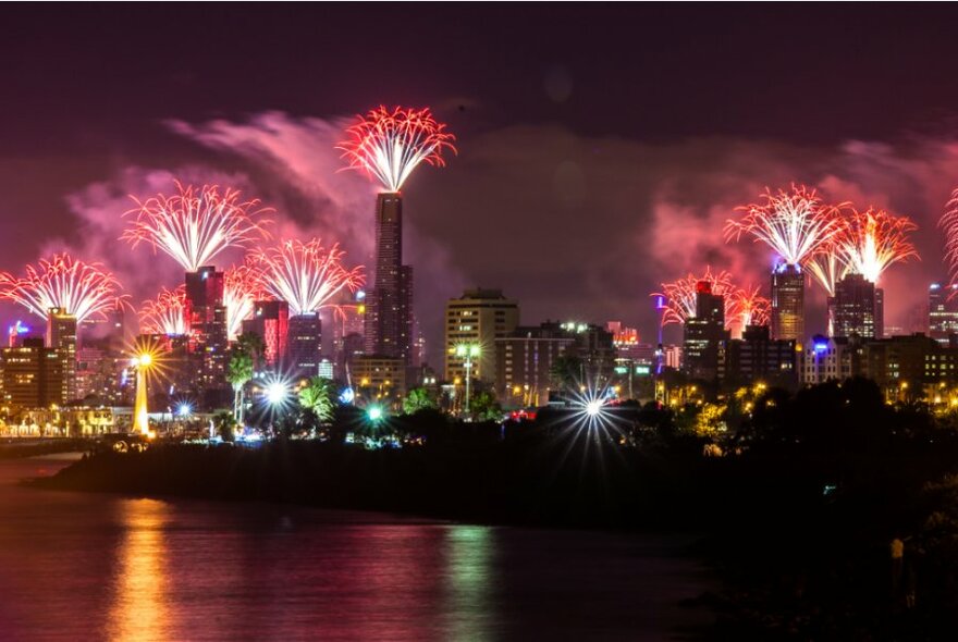 Nighttime with Yarra River in foreground and illuminated banks of city skyline in background with firework displays.