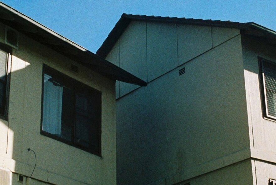 Two fibro dwellings, seen from below, against a blue sky background.
