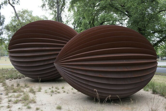 Two large pod-like steel sculptures in parkland.