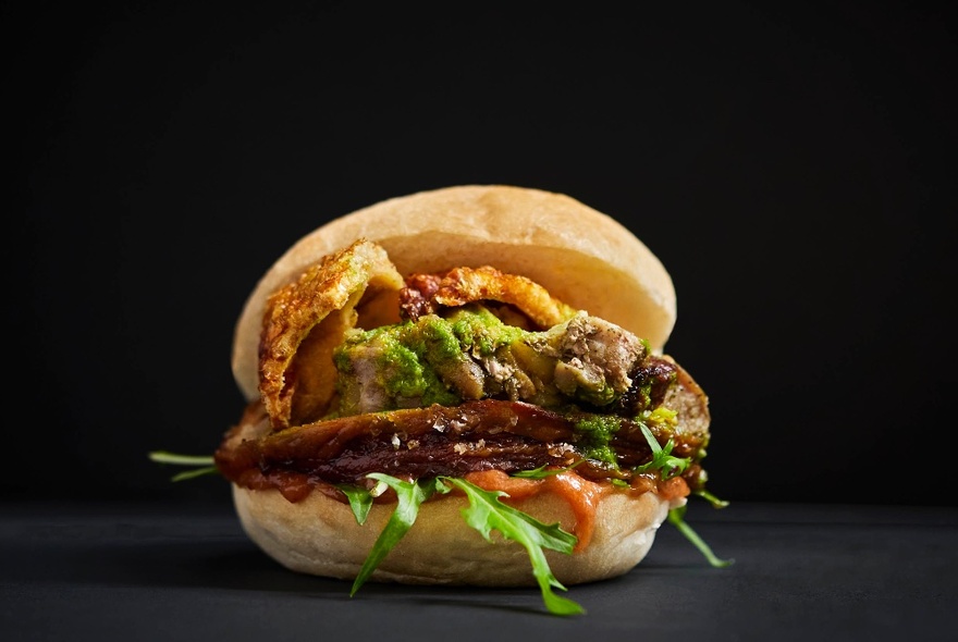 A  burger filled with grilled meat and salad, against a dark background.