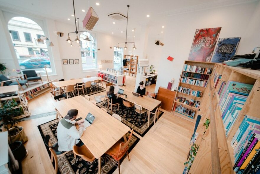 Overhead view of writing studio with shelves lined with books and people seated at wooden tables with laptops.