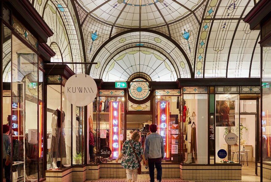 Two people are walking in an arcade with a stained glass window ceiling