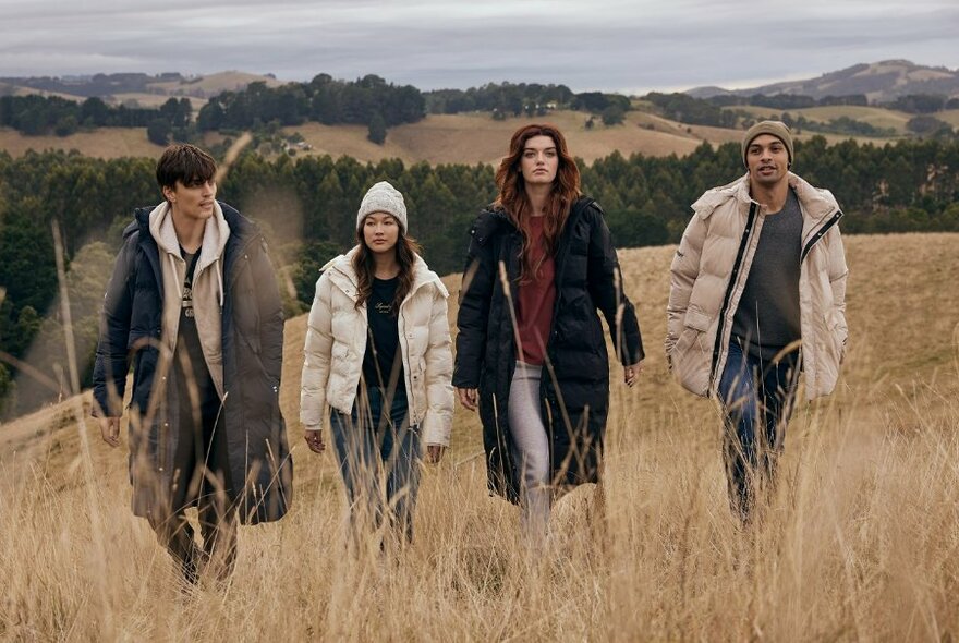 Four male and female models in a cold outdoor setting wearing puffer jackets, long coats and beanies.