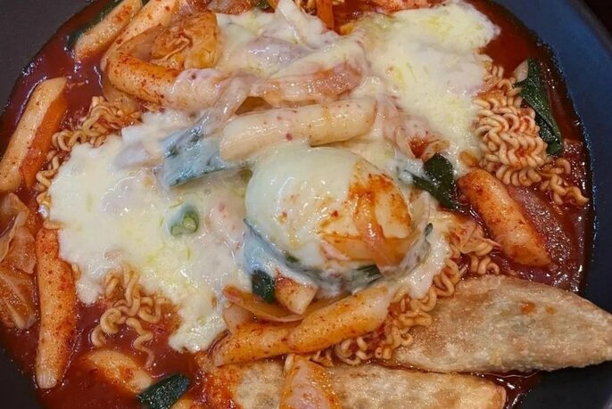 Close up of red dish with noodles and egg, covered with cheese.