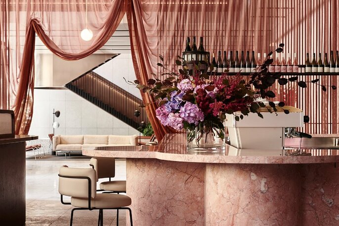 Dame's pink marble bar topped with a huge vase of flowers, in front of pink draped curtains.