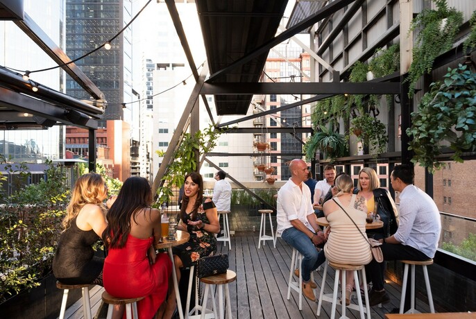 Rooftop terrace with patrons sitting on stools and greenery on the walls.