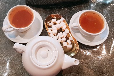 Looking down at two cups of tea and a teapot with cubes of sweets. 