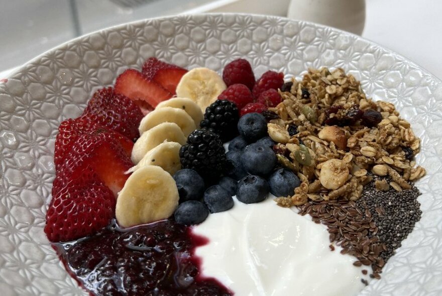 A bowl of muesli, fresh fruit, yoghurt and stewed berries.