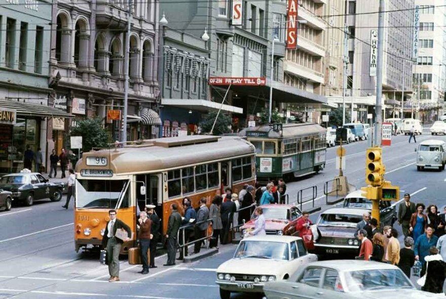 An old photo of a yellow tram on a city street.