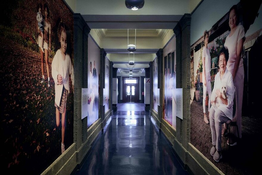 Looking down a dim corridor with large family portraits on the walls.