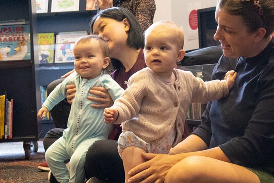 Babies sitting with their carers in a library.
