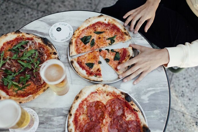 Three pizzas on a small table, with a hand holding a slice