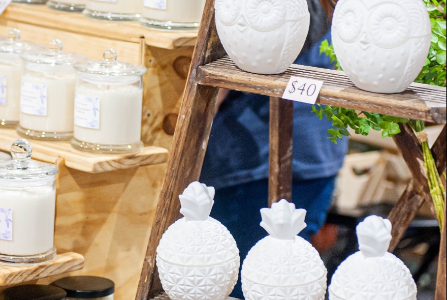 Products on display at a market stall, including white ceramics and candles in glass jars.