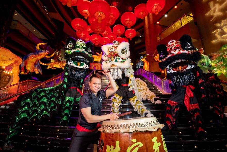 Perfomer standing next to a large drum and the head of a large dragon puppet and Chinese zodiac installation inside the Atrium at Crown Melbourne.