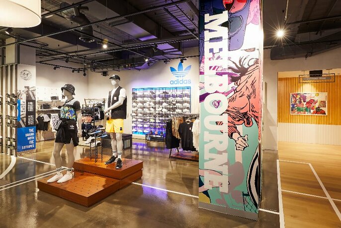 Interior of an Adidas store with mannequins wearing sports clothing, a wall of sneakers and a large banner reading Melbourne