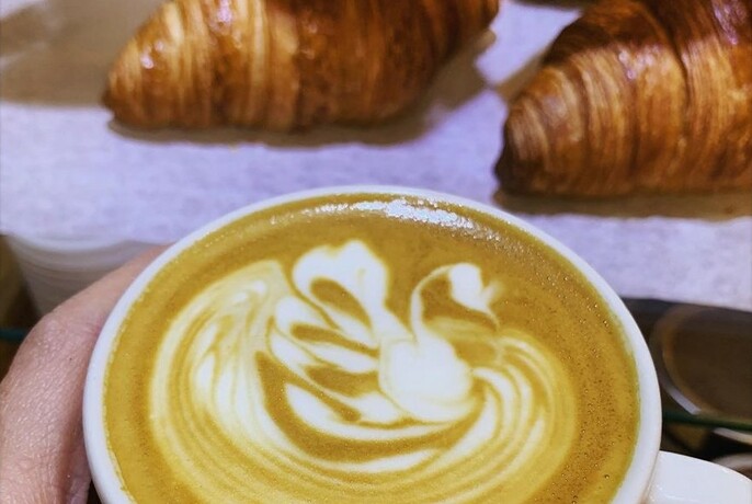 Close-up of a cup of coffee with two croissants in the background.