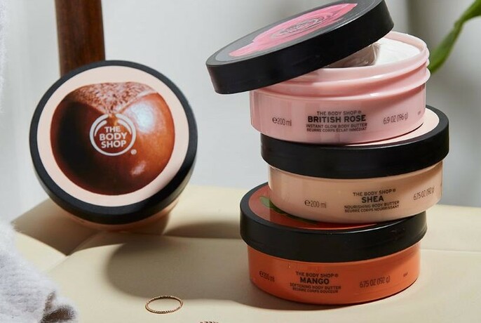 A stack of three Body Shop tubs with one, lid up, to the left. 