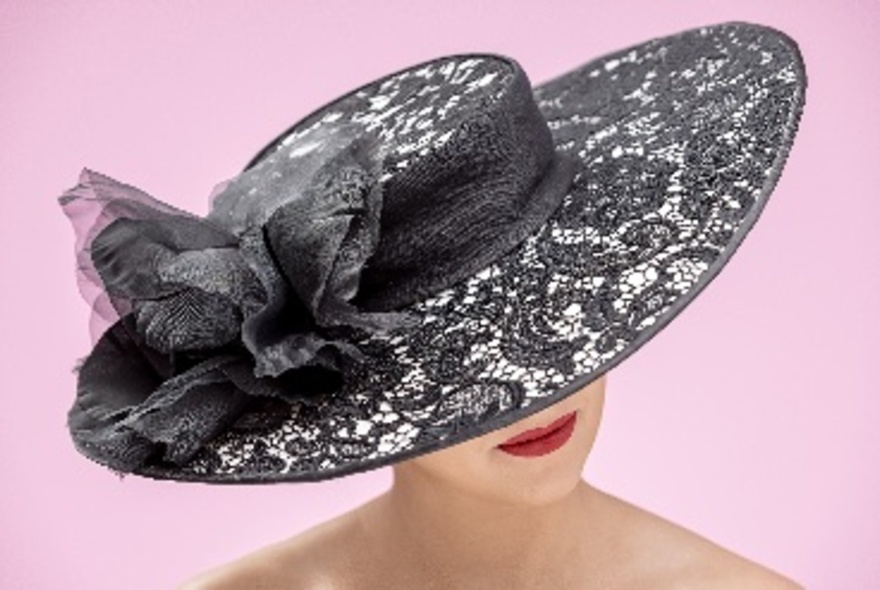 Model wearing a black lace Spanish-style hat against a pink background.