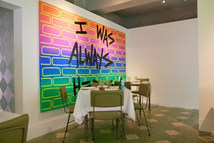 A simple table in a restaurant in front of a coloured mural. 