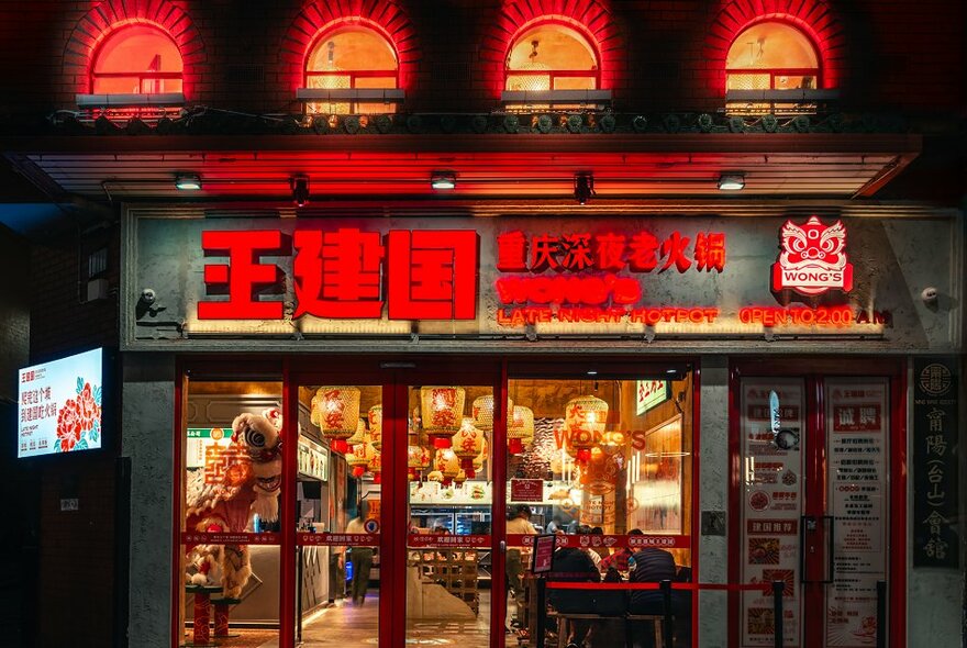 Exterior view of the shopfront of Wong's Hot Pot at night, showing red signage and large windows onto the street.