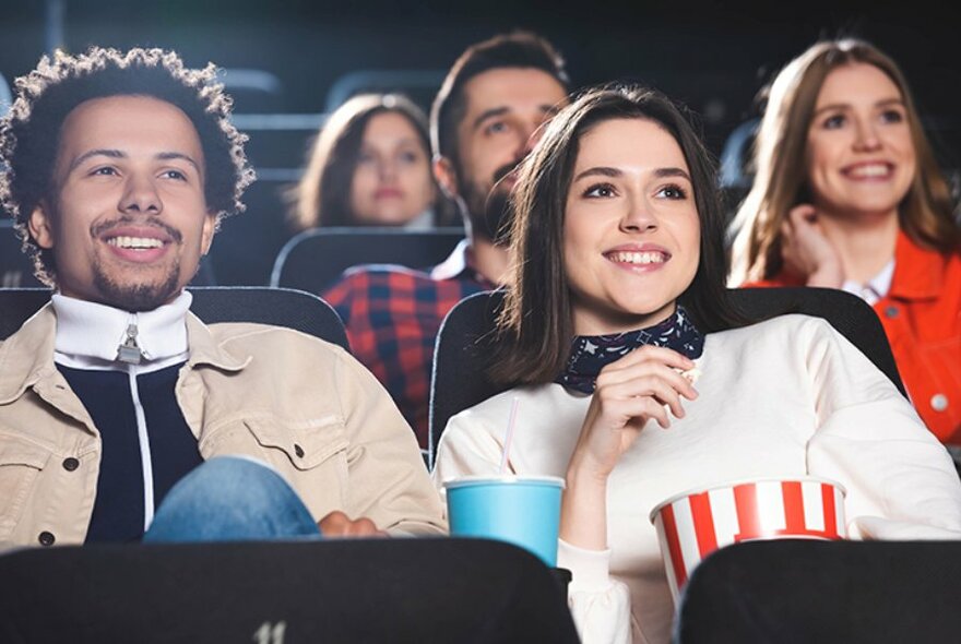 Young smiling people in a cinema enjoying a movie with popcorn and drinks. 