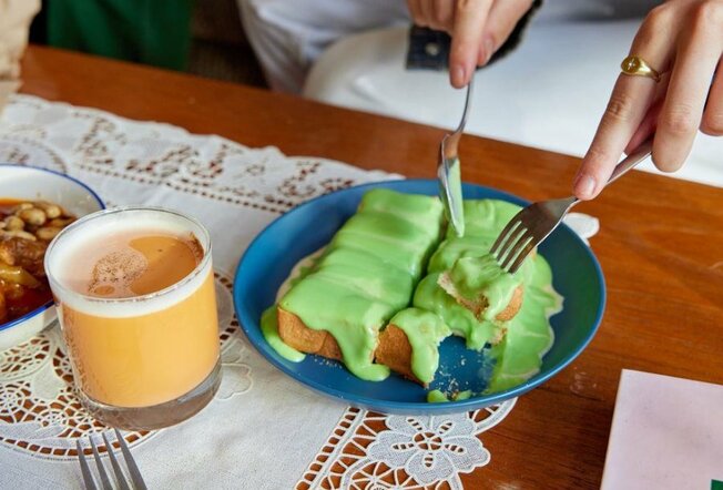 A piece of toast with green jam on top next to a cup of milk tea