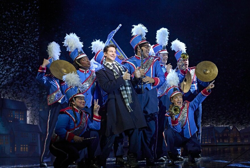 The cast from the musical Groundhog day on stage; a group of them in marching band costumes with instruments surrounding a man in a suit and coat. 