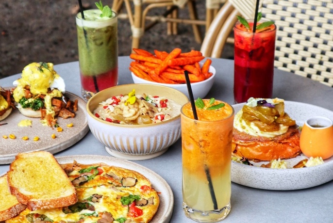 Table full of breakfast dishes and colourful drinks in tall glasses.