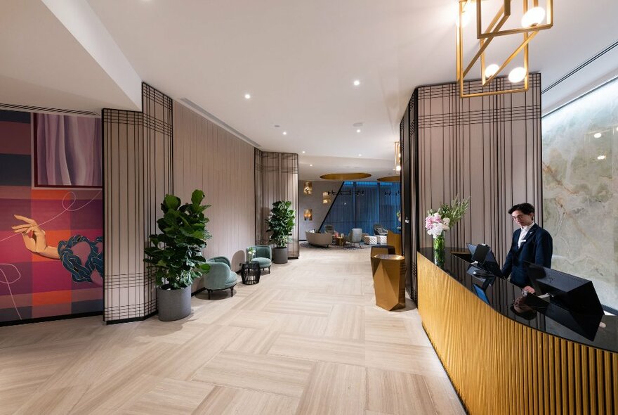 Spacious lobby of Dorsett Melbourne showing front desk, armchairs, plants and artwork on the walls. 
