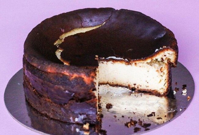 A burnt Basque cheesecake on a silver cake board, with a slice cut out.