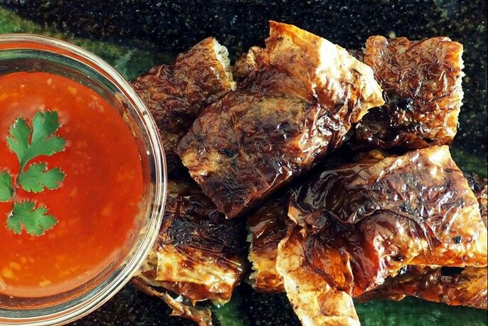 A plate of charred chicken with a bowl of red dipping sauce garnished with coriander. 