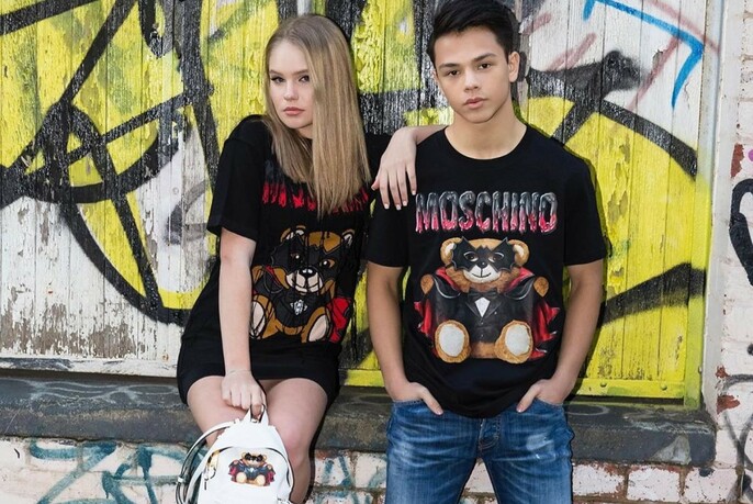 Two young people in Moschino T-shirts in front of a graffiti-covered wall.