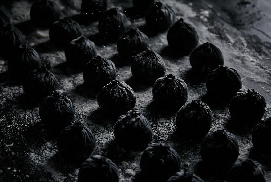 Rows of  many black dumplings with twisted tops.