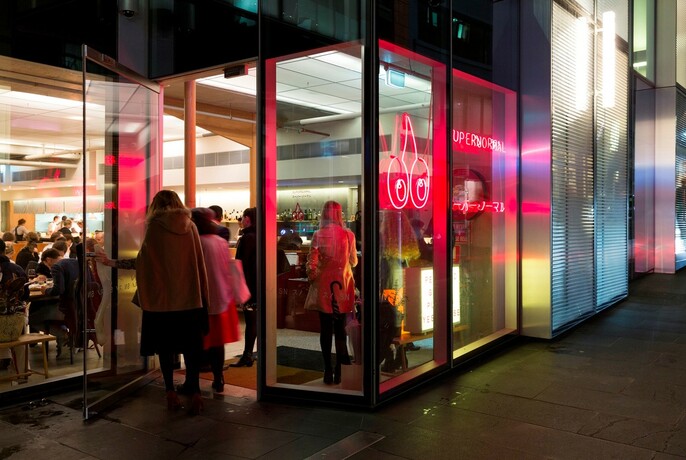 People entering a restaurant at night with red neon signage.