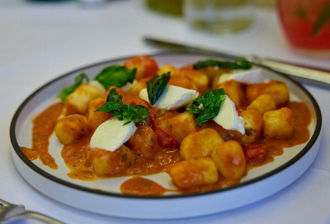White plate with black rim, gnocchi in Napoli sauce with basil leaves and bocconcini on top.
