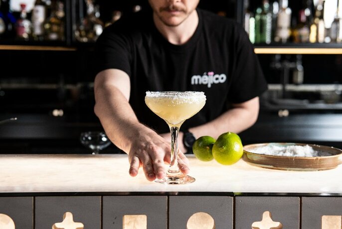 A bar tender pushing a large margarita to the edge of a bar.
