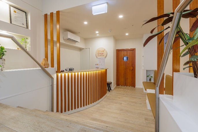 Tranquil foyer and reception desk at a massage studio, with white walls, wooden feature panels and pale flooring. 