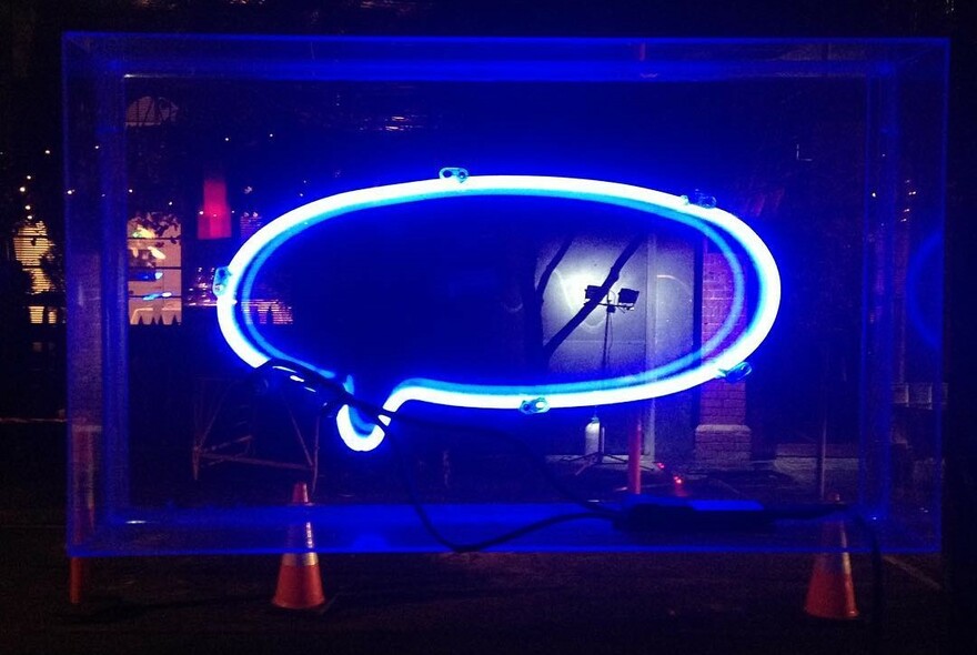 Neon sign, shaped like a speech bubble, lit up at night in a bar window. 