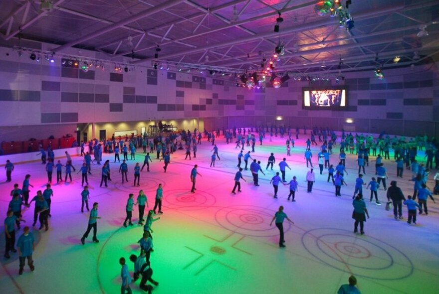 People skating in an indoor ice rink with disco lighting.