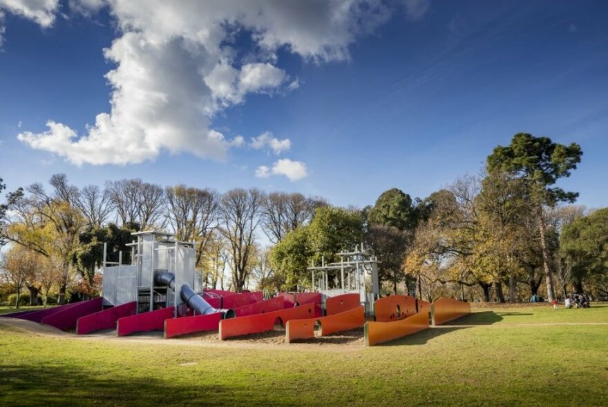 A playground with red and orange walls forming a maze in a green park. 