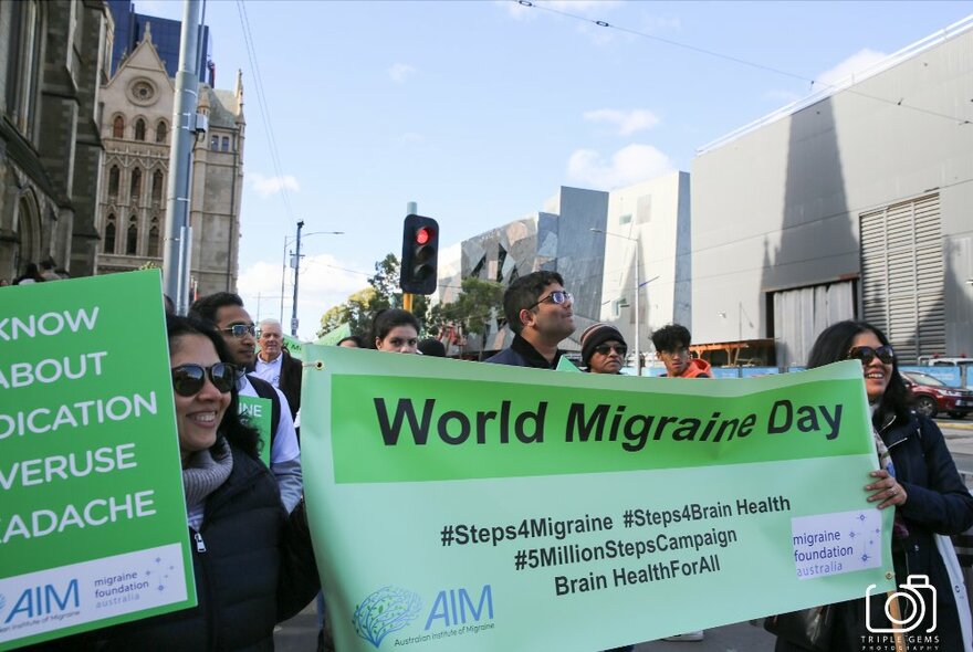 People gathered opposite Fed Square holding banners for World Migraine Day.