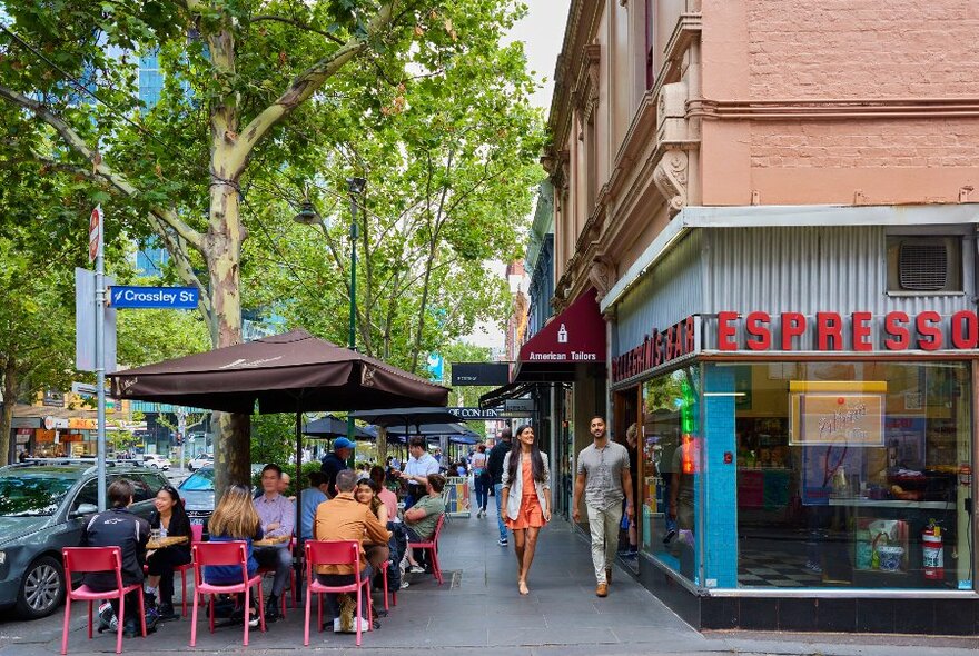 Two people are walking past an Italian restaurant there are people sitting outside under umbrellas